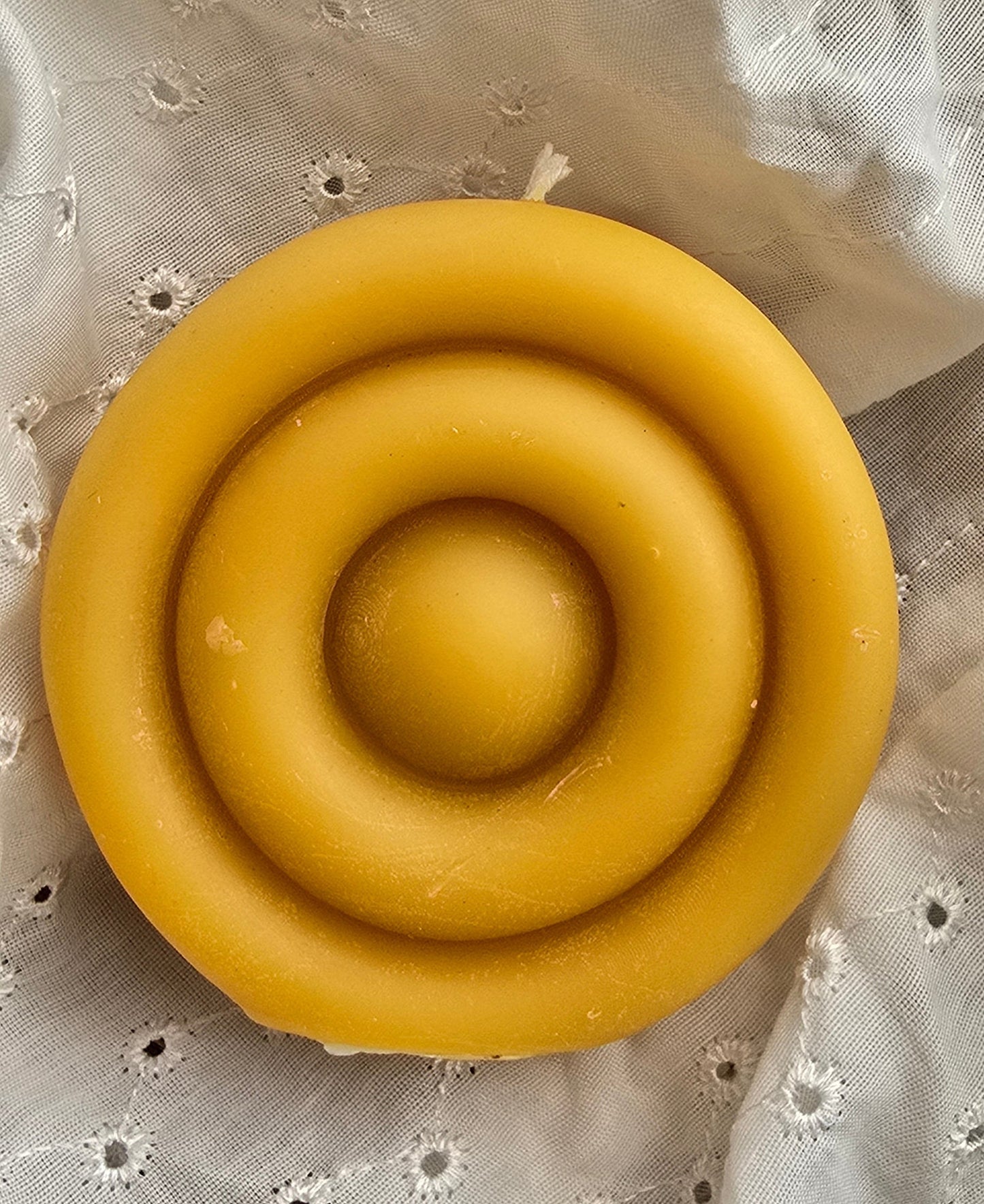 Beeswax candle with concentric circles on a white lace fabric background