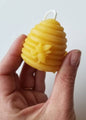 Hand holding a yellow beehive-shaped candle against a light background